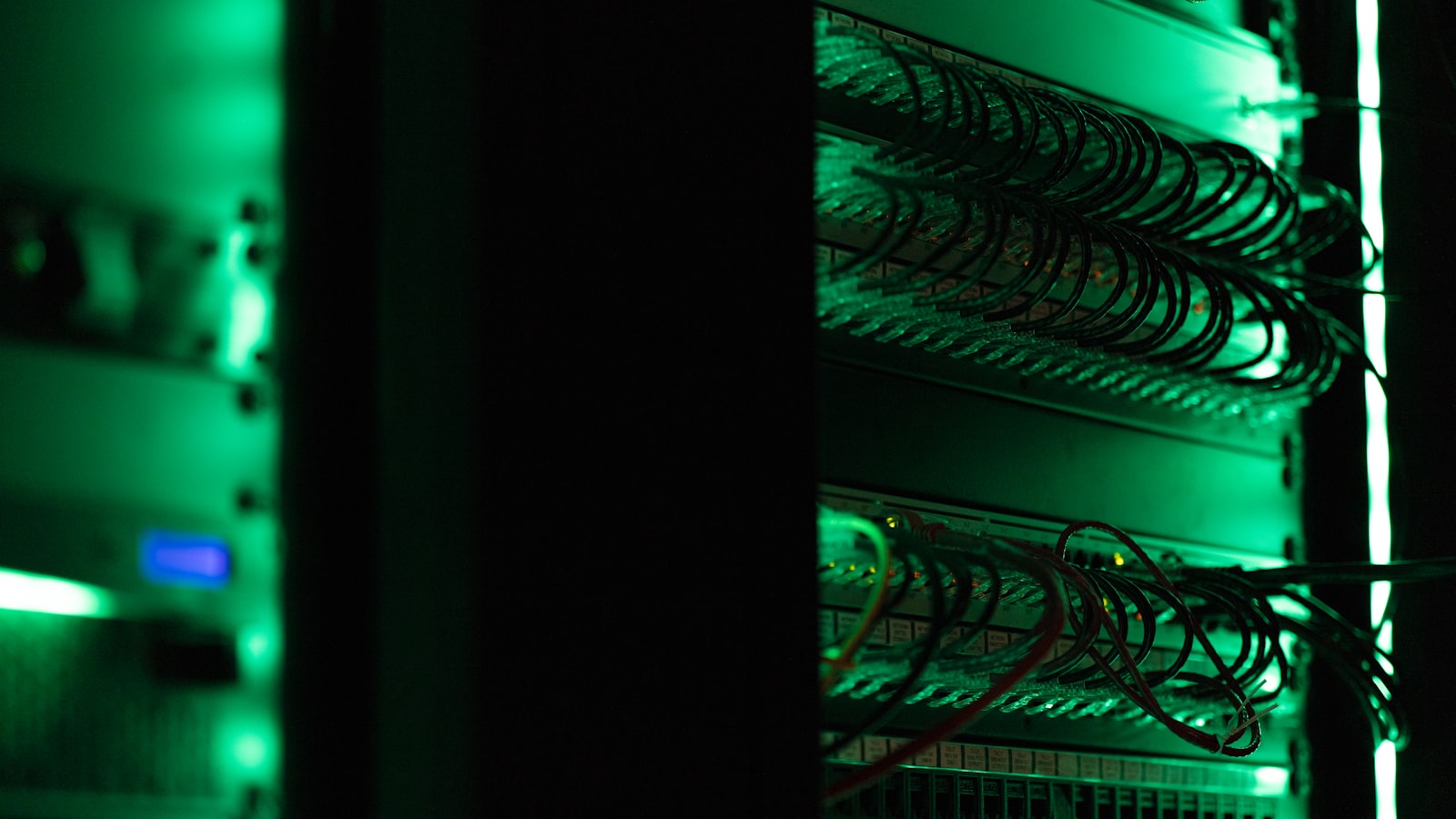 A dark server rack lit by green status LEDs and bundled cabling
